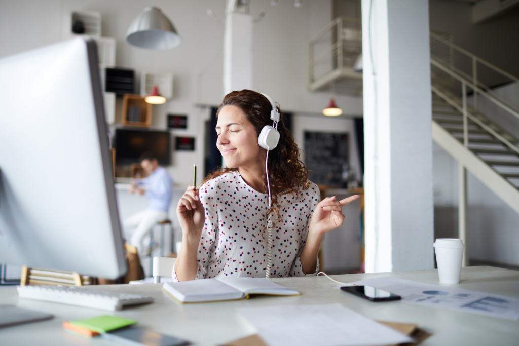Woman at a desk, dancing to music from headphones