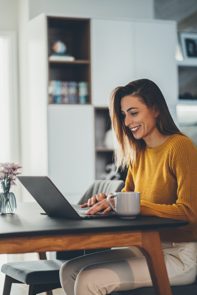 Woman at a table working on her computer and smiling